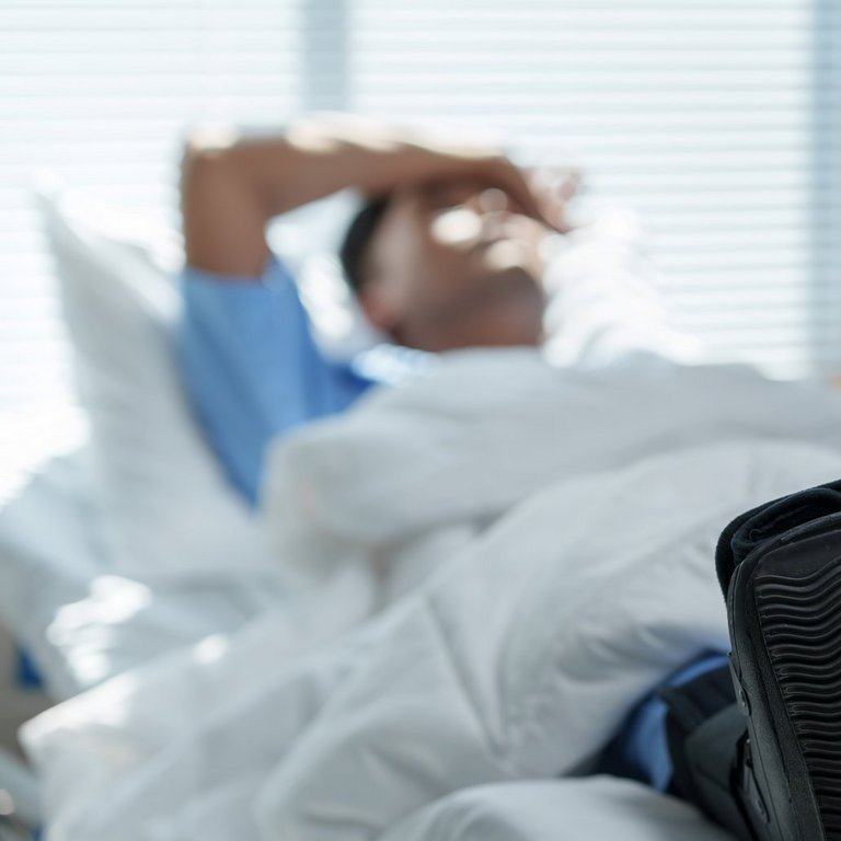 Patient recovering in hospital bed with walking boot: dealing with foot or ankle injury Eine medizinische Fachkraft im AKH Celle justiert eine Infusion. Im Hintergrund ist eine verschwommene Person zu erkennen.