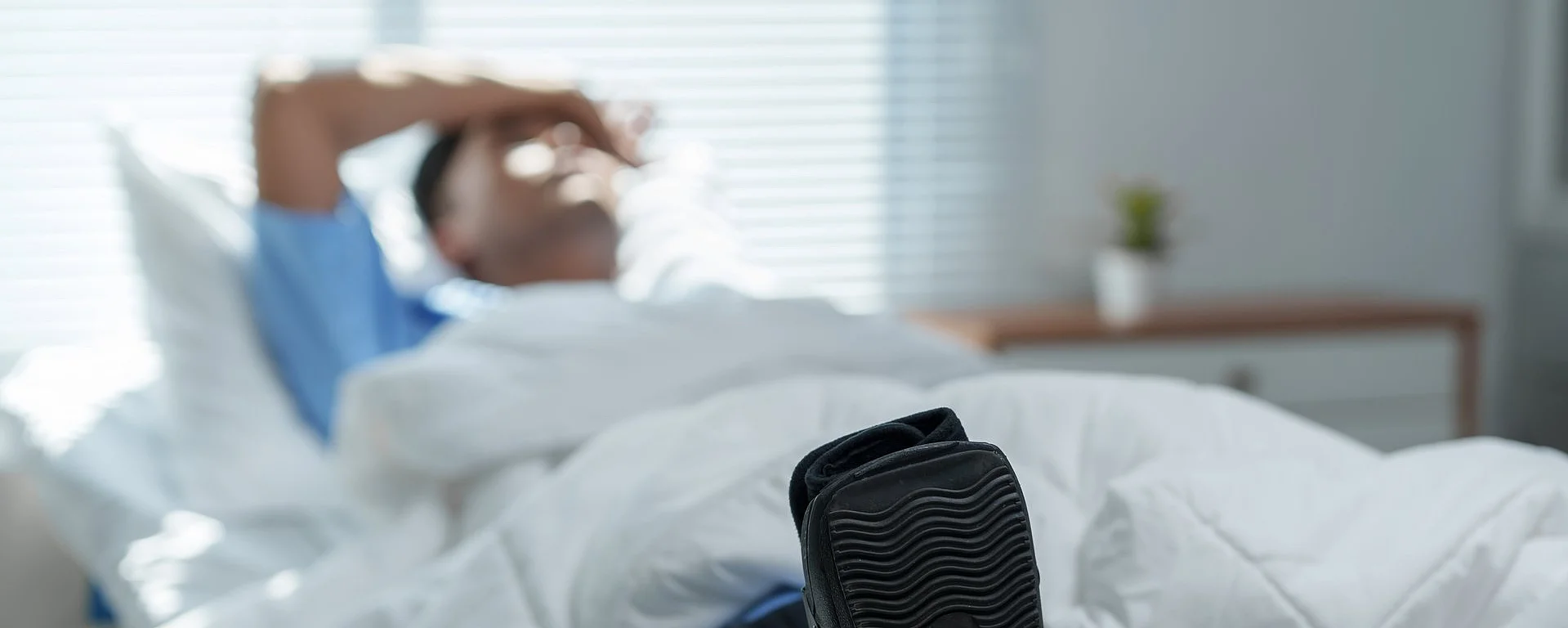 Patient recovering in hospital bed with walking boot: dealing with foot or ankle injury Eine medizinische Fachkraft im AKH Celle justiert eine Infusion. Im Hintergrund ist eine verschwommene Person zu erkennen.