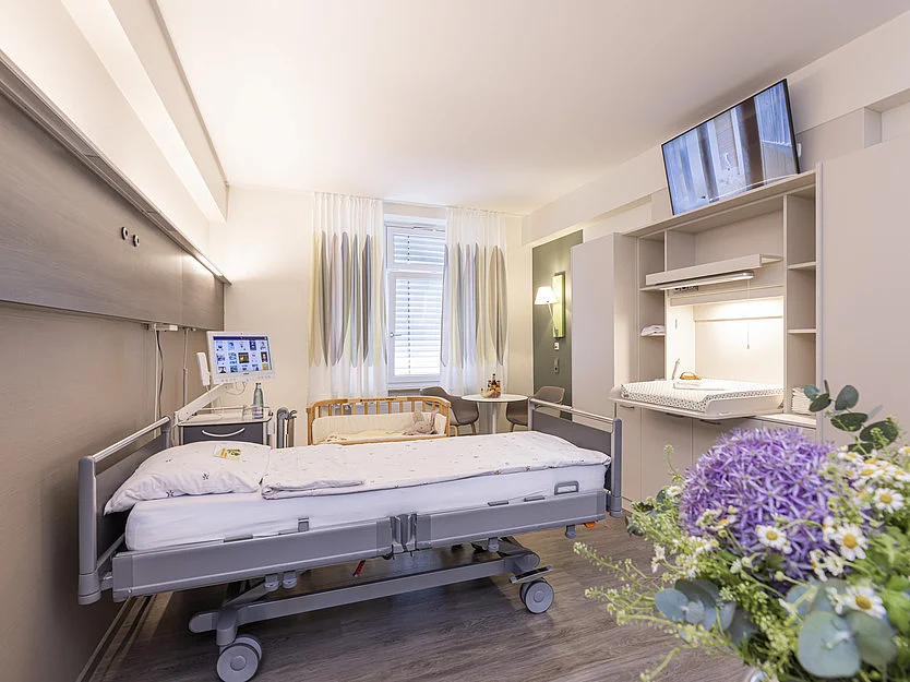 Komfortables Einbettzimmer auf der Geburtsstation mit moderner Ausstattung und Blumenstrauß.