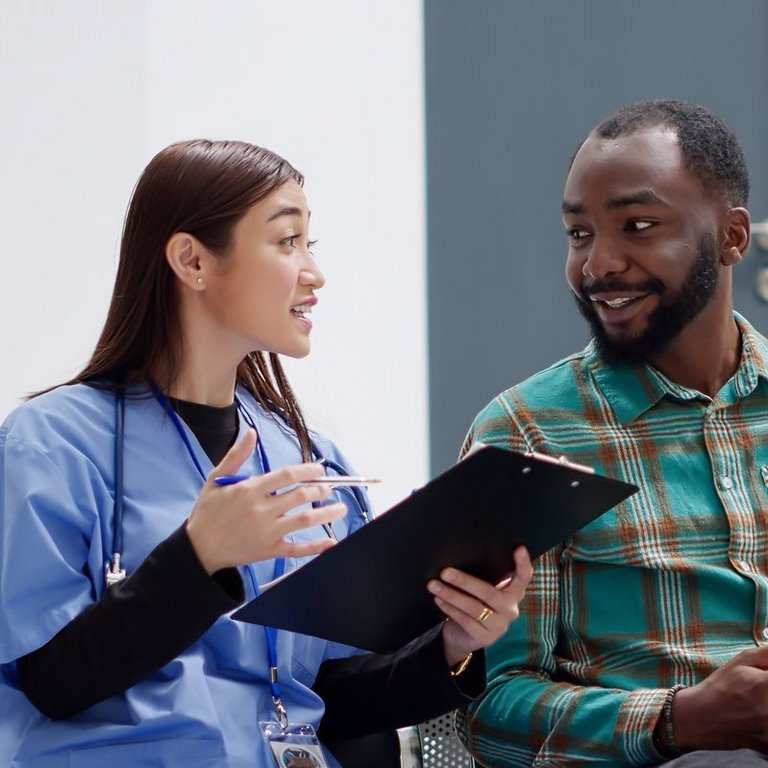 Medizinische Fachkraft bespricht mit männlichem Patienten ein Formular im Wartebereich einer Klinik