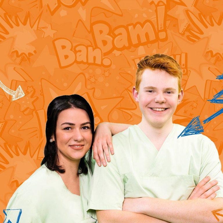 Zwei Jugendliche in OP-Kleidung stehen lachend vor einem orangefarbenen Hintergrund mit Comic-Grafiken.