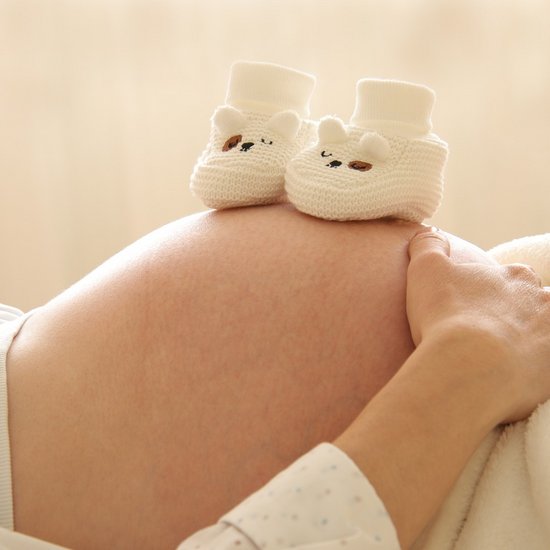 Eine schwangere Frau mit Babyschuhen auf ihrem Bauch 