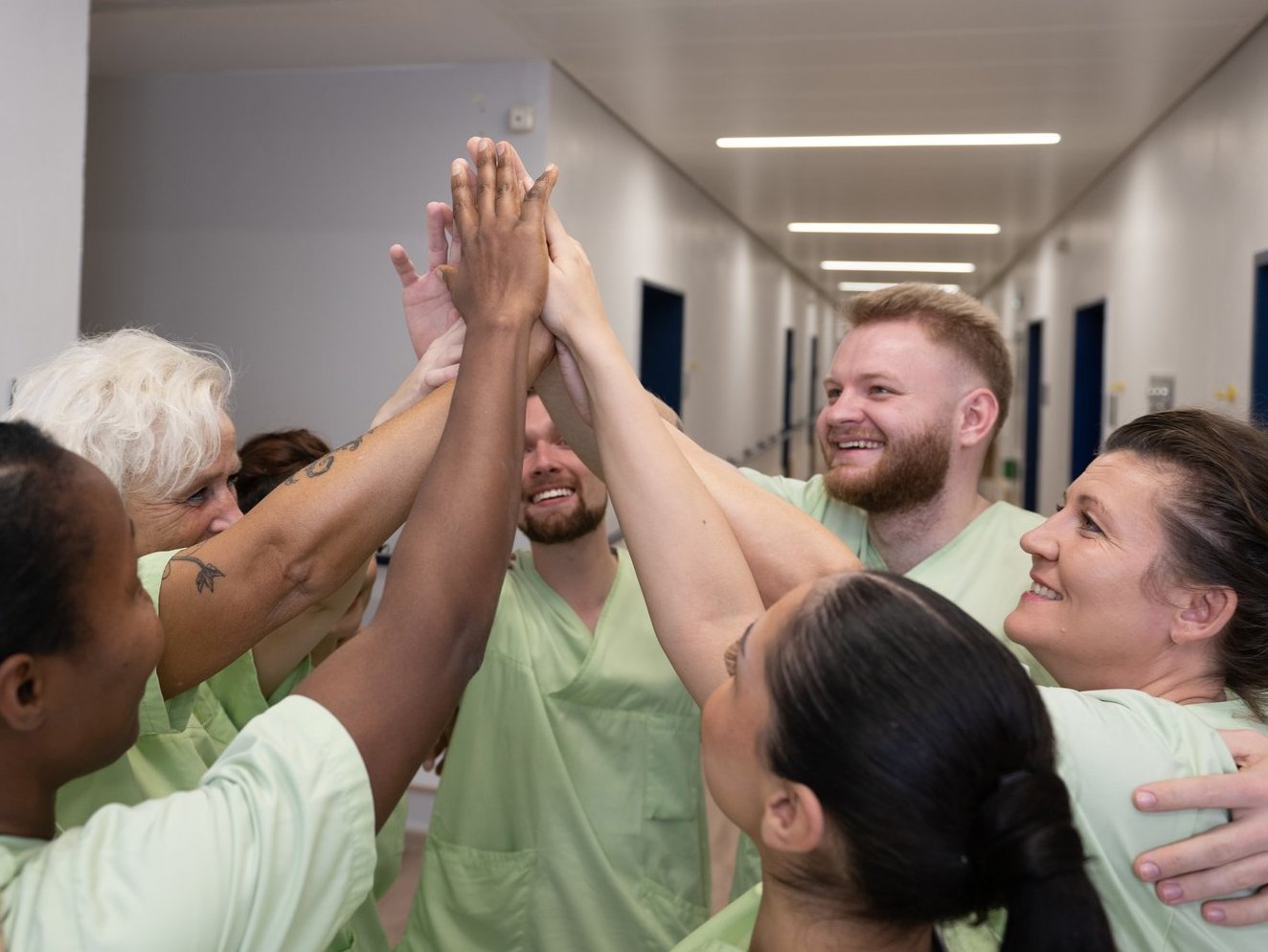 Ein Team von Pflegekräften steht in einem Flur und gibt sich gemeinsam ein motivierendes High-Five.