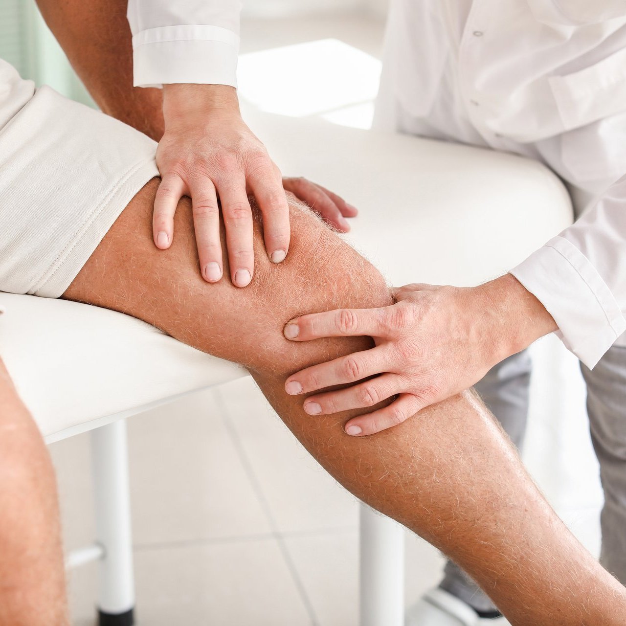 Ein Arzt untersucht das Knie eines Patienten – Fokus auf Schmerzdiagnostik oder orthopädische Behandlung.