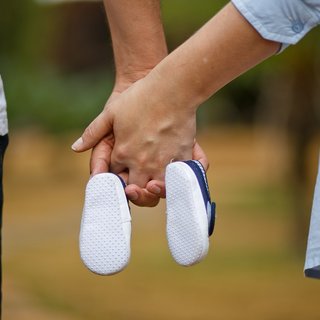 Eltern halten Händchen und tragen Babyschuhe in ihren Händen.