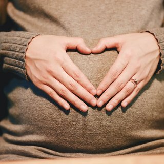 Eine schwangere Frau formt mit ihren Händen ein Herz vor dem Bauch