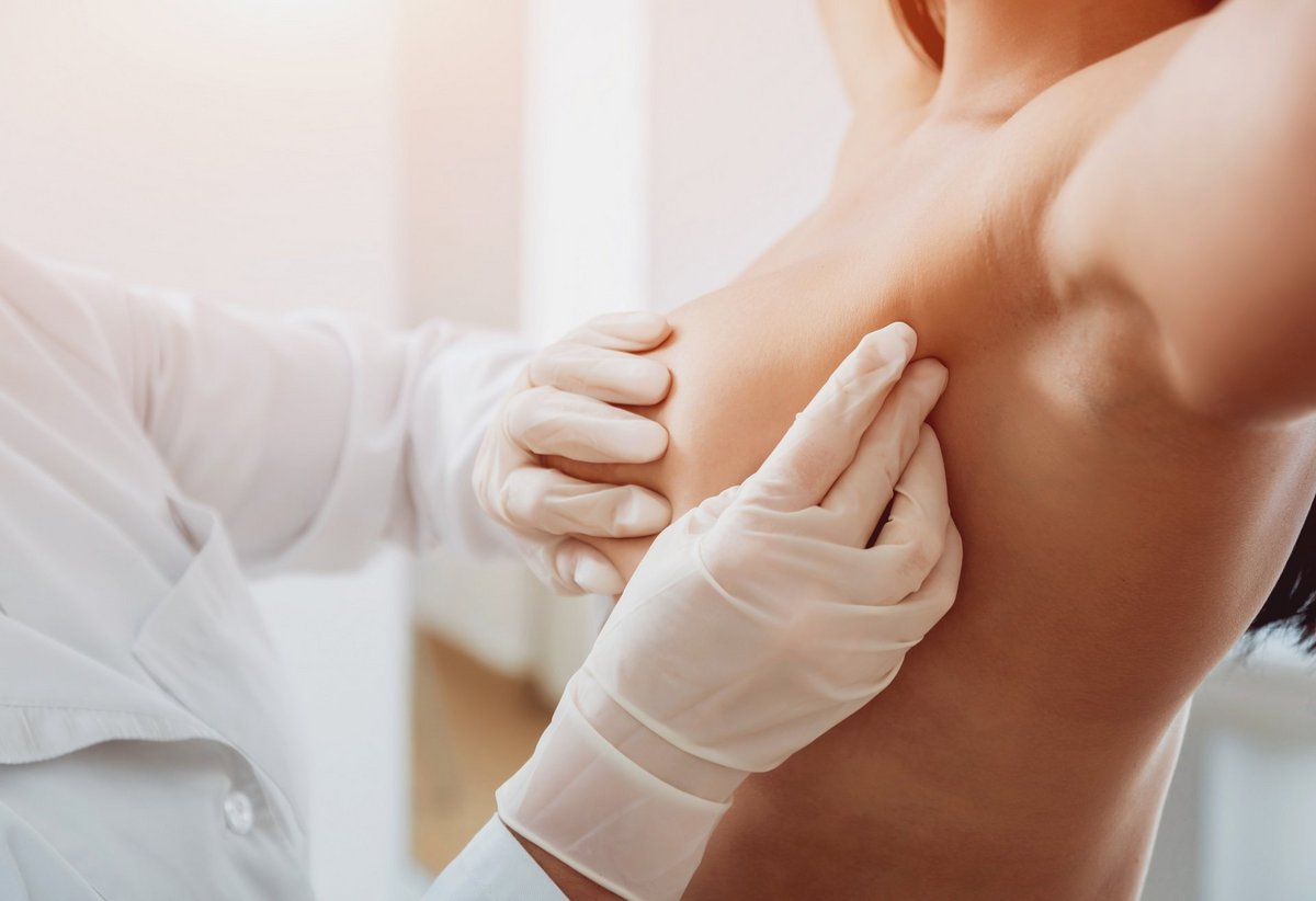 Ein Arzt tastet die Brust einer weiblich wirkenden Person ab.