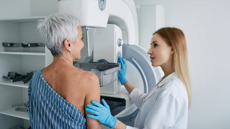 Ärztin betreut eine Patientin während einer Mammographie-Untersuchung und positioniert sie sorgfältig am Gerät.