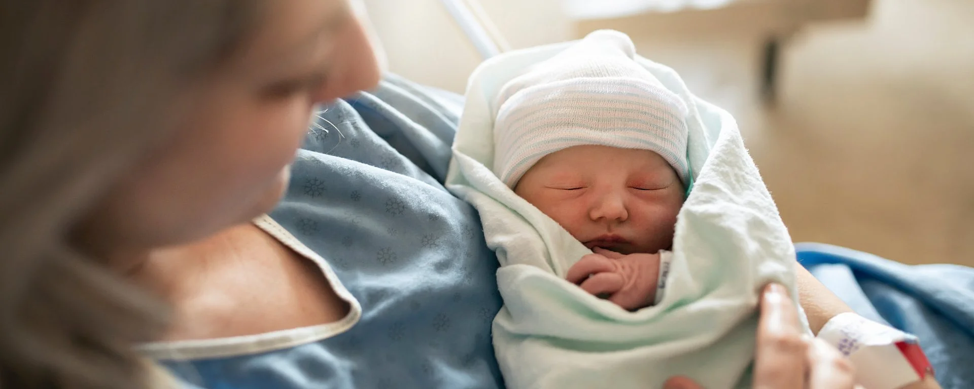 Neugeborenes liegt nach der Geburt eingewickelt im Arm der Mutter im Krankenhausbett