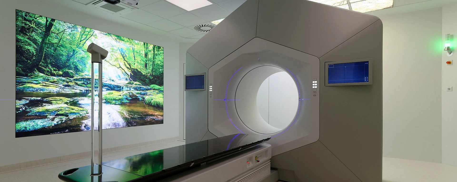 Moderner Behandlungsraum mit großem Strahlentherapiegerät und beruhigender Naturprojektion an der Wand.
