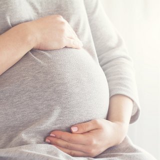 Eine schwangere Frau hält ihren Bauch mit beiden Händen