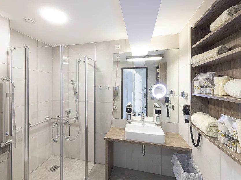 Modern ausgestattetes Badezimmer auf einer Geburtsstation mit barrierefreier Dusche.
