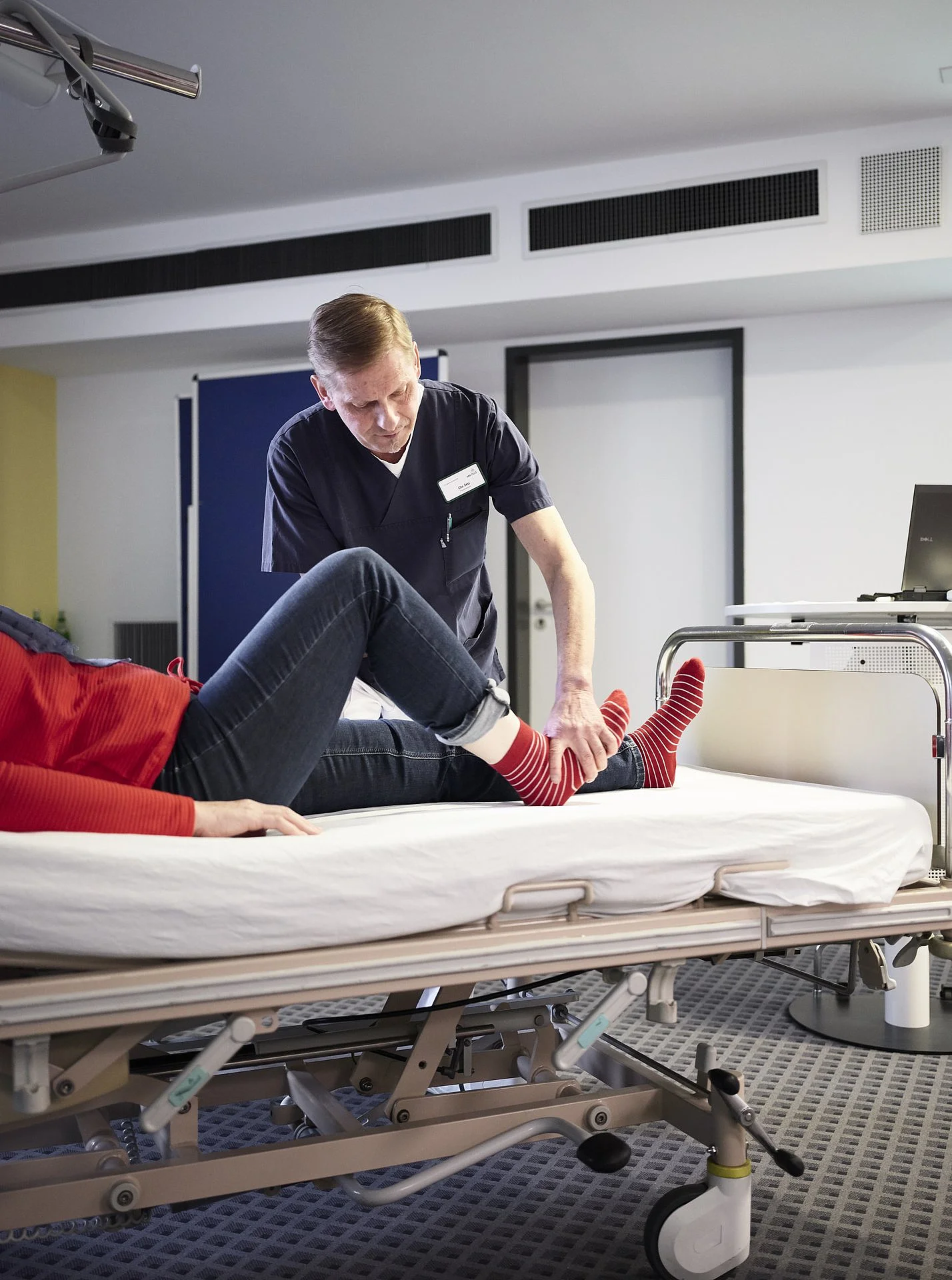 Therapeut unterstützt eine Patientin bei einer Beinübung im Klinikbett.