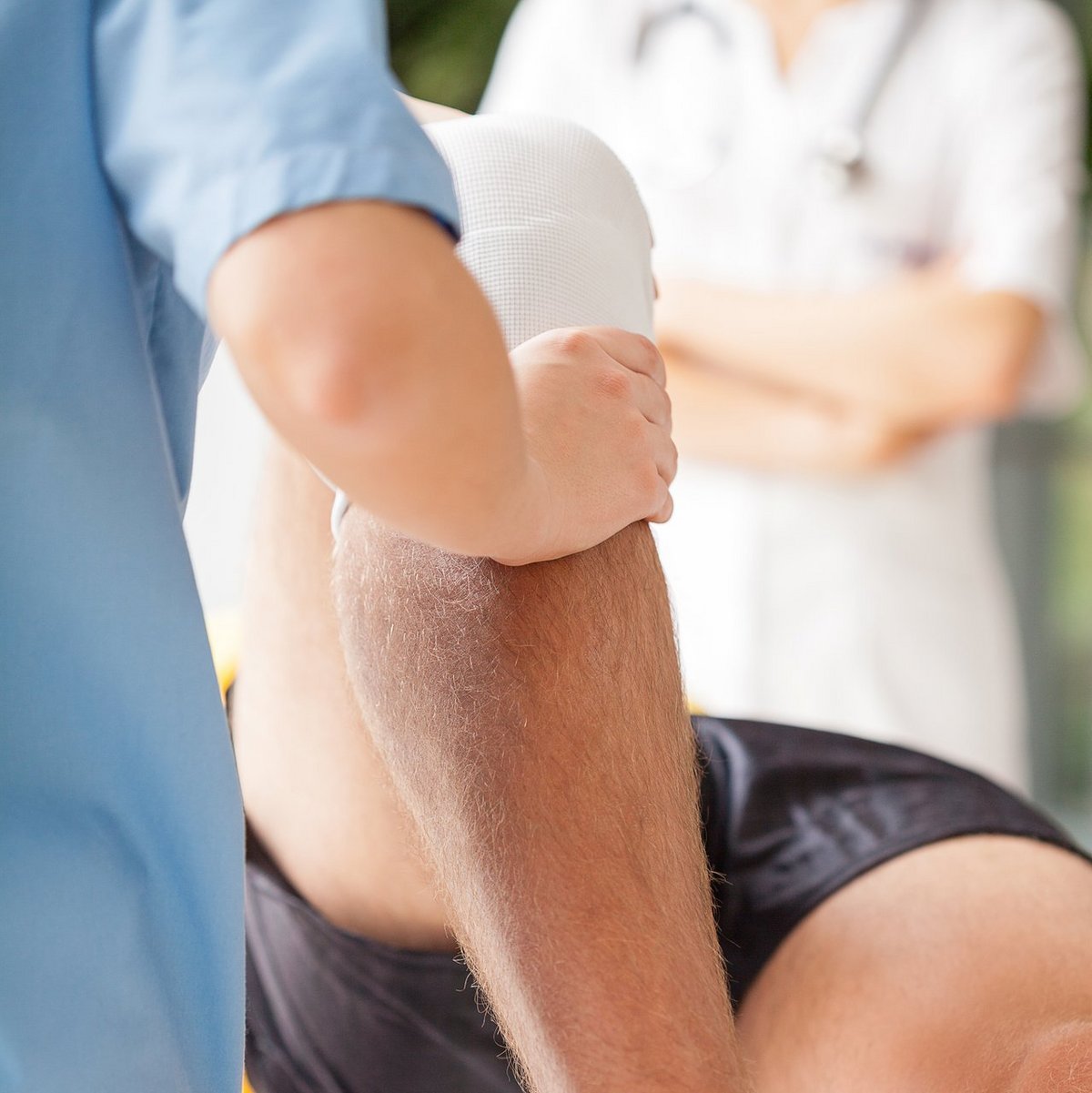 Consulting room Physiotherapeutin mobilisiert bandagiertes Knie eines männlichen Patienten während Rehabilitationsbehandlung