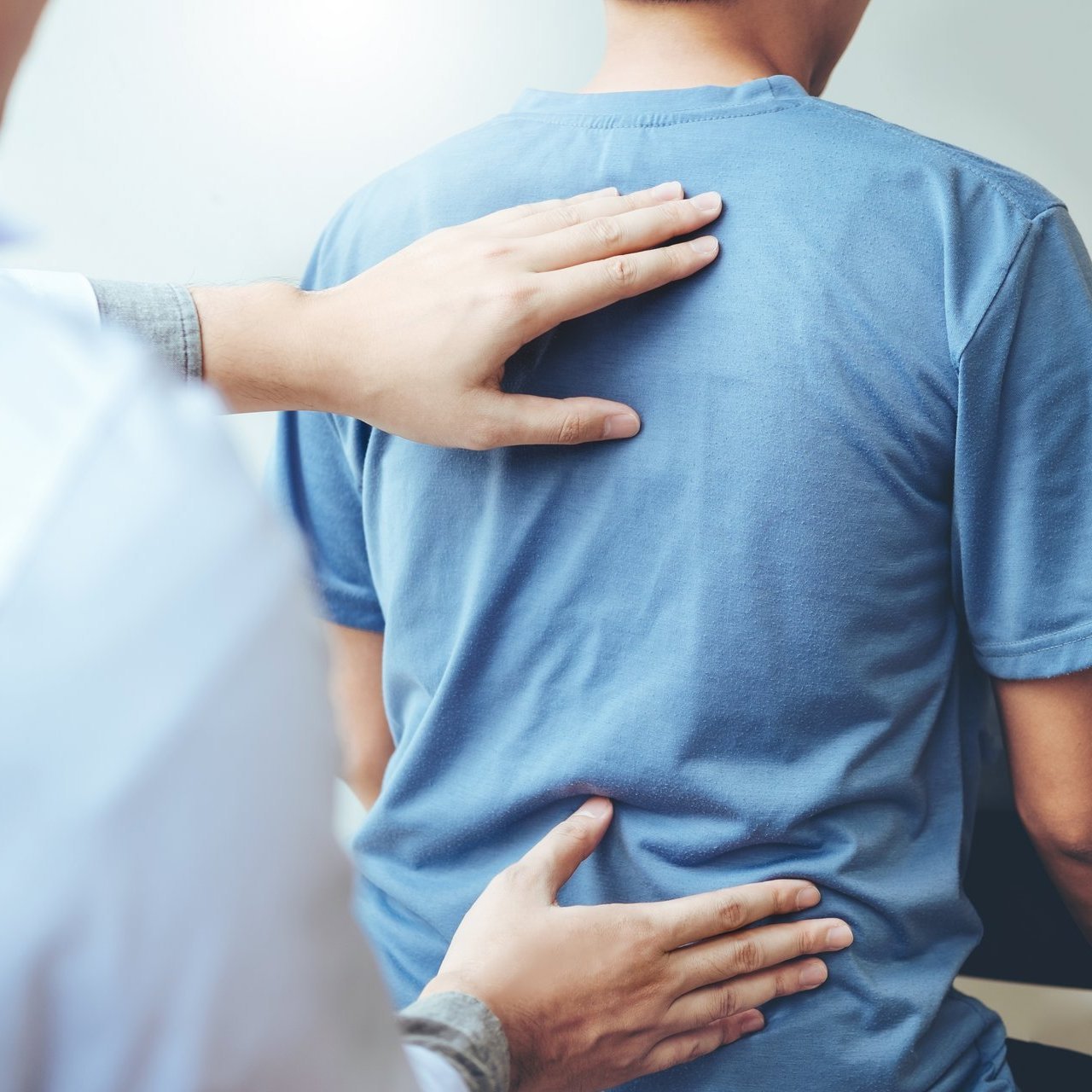 Ein Arzt untersucht den Rücken eines Patienten, vermutlich zur Abklärung von Schmerzen oder Beschwerden im Wirbelsäulenbereich.