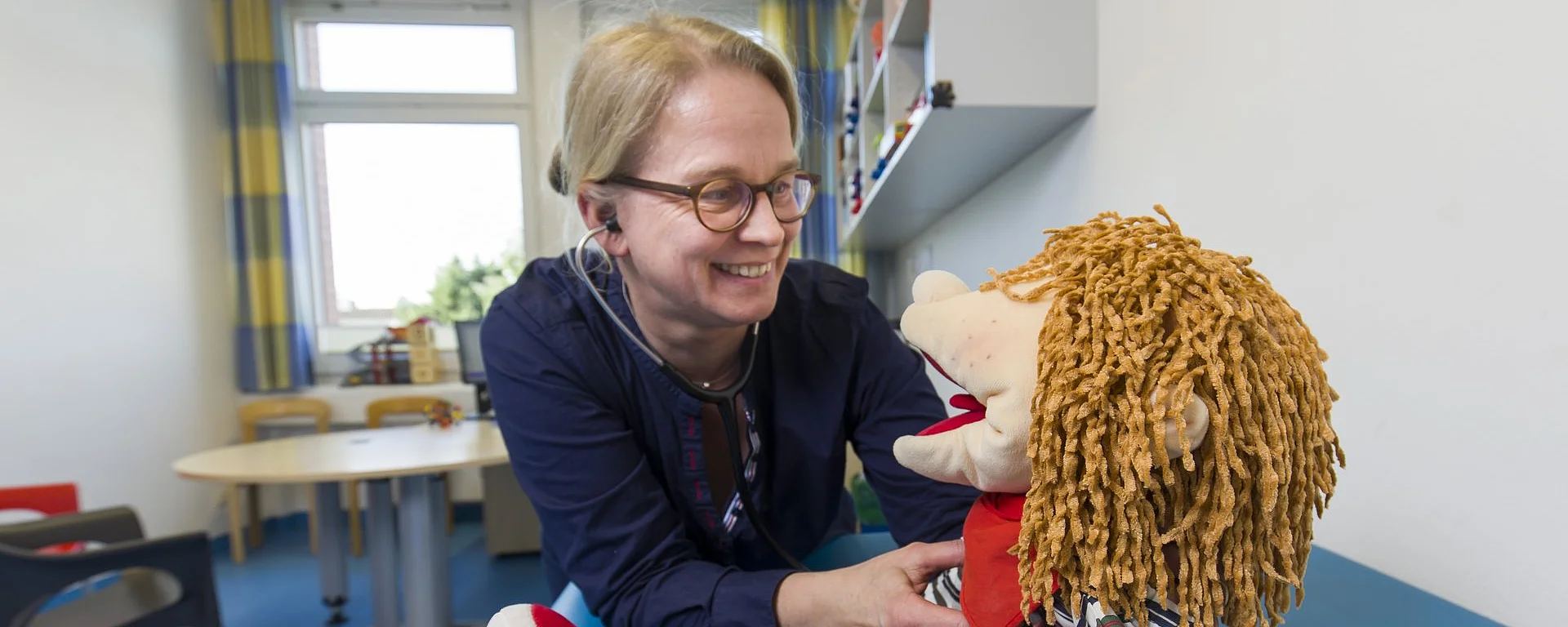 Therapeutin spielt mit einer Handpuppe in einem freundlich eingerichteten Kindertherapieraum.