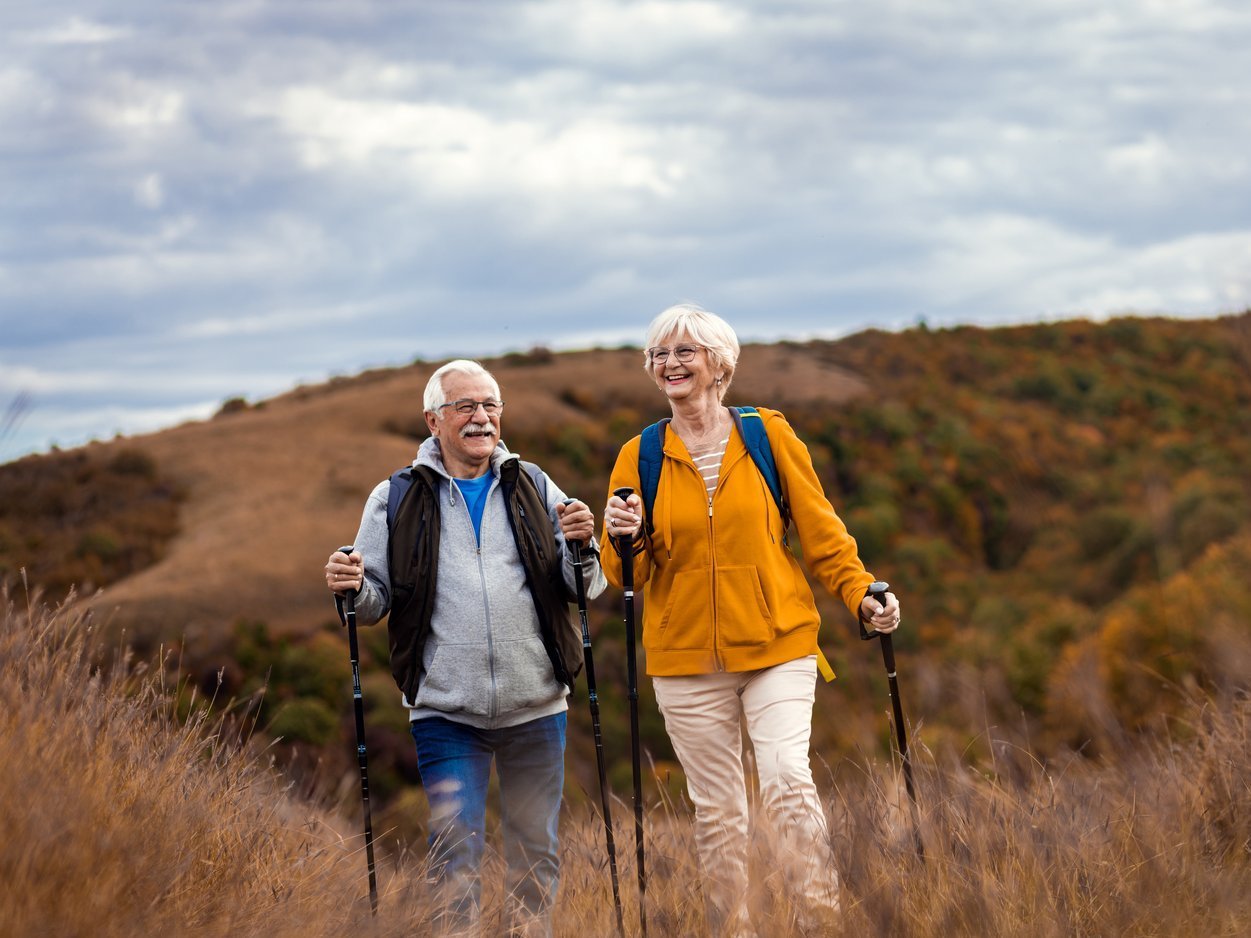 Älteres Paar beim Wandern mit Trekkingstöcken in herbstlicher Hügellandschaft