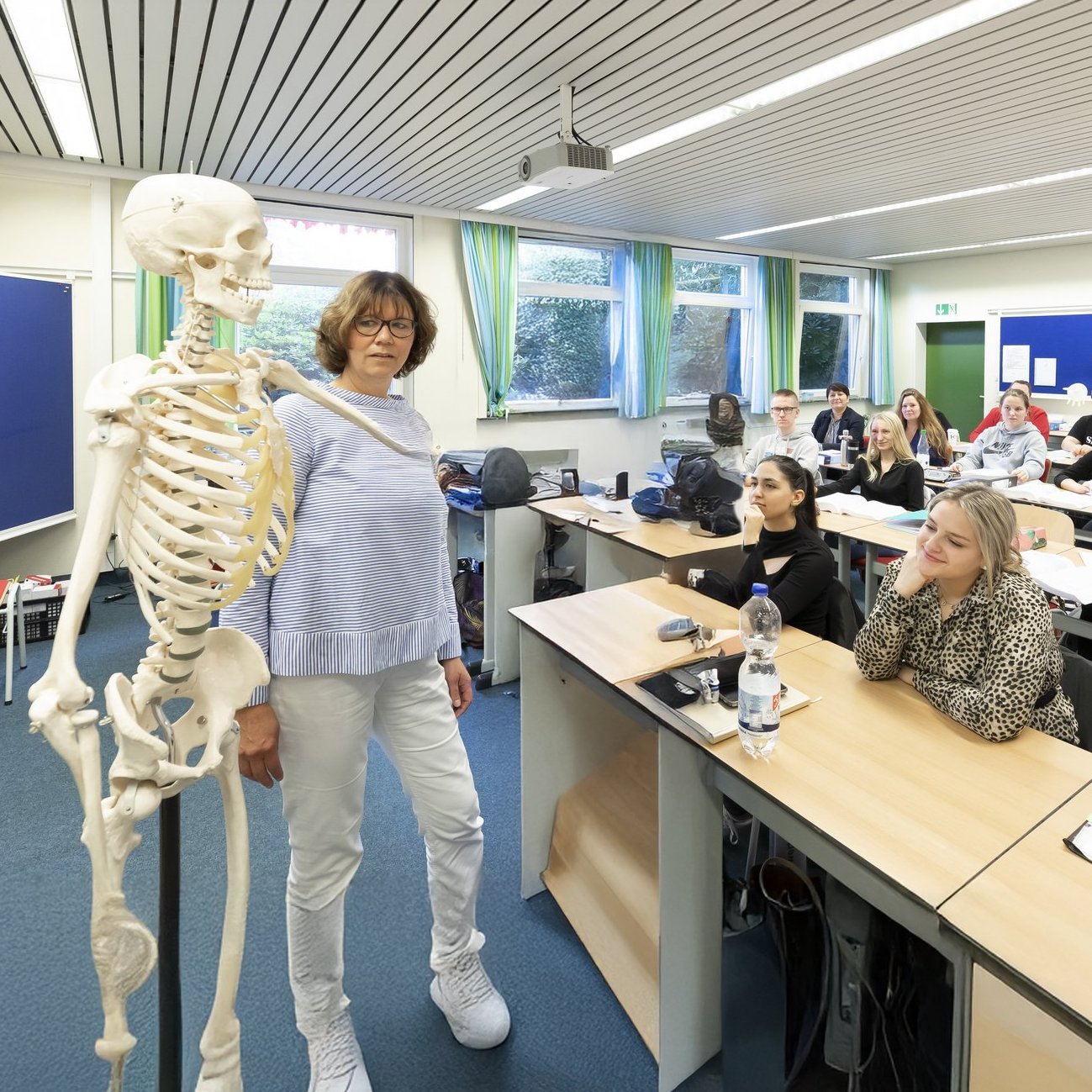 21-09-29-akh-057 Die Szene zeigt einen lebendigen Unterricht im medizinischen Bereich: Eine Lehrkraft erklärt anatomische Zusammenhänge am Skelettmodell, während die Studierenden aufmerksam folgen.