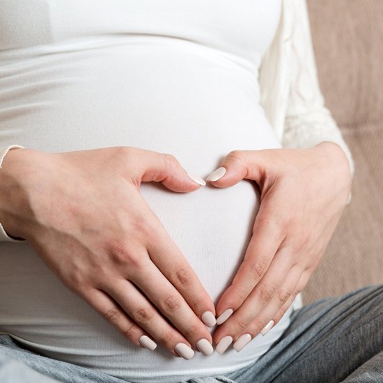 Young pregnant woman holds wooden heart. Love concept Eine schwangere Frau formt mit ihren Händen ein Herz und hält diese an ihren Bauch.
