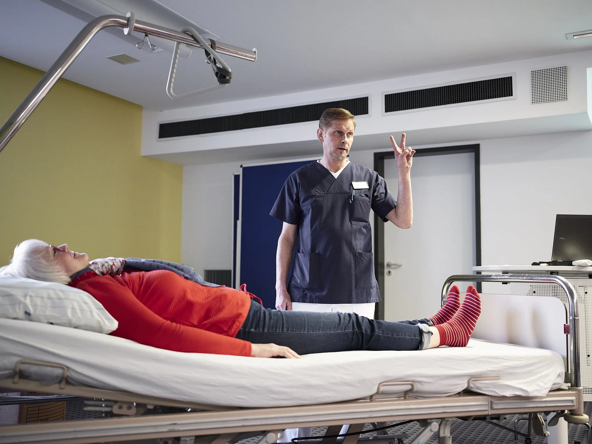 Therapeut führt eine Mobilisationsübung mit einer älteren Patientin im Klinikbett durch.